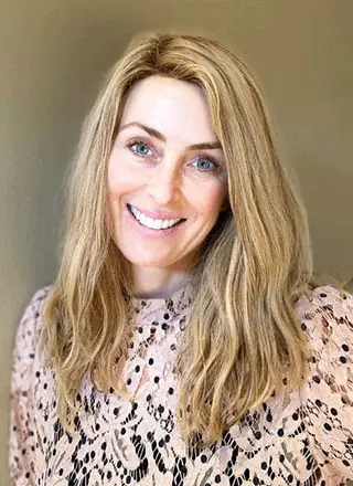 Headshot of Dr. Anne Scott wearing a lace top and black inner against a brown plain background.